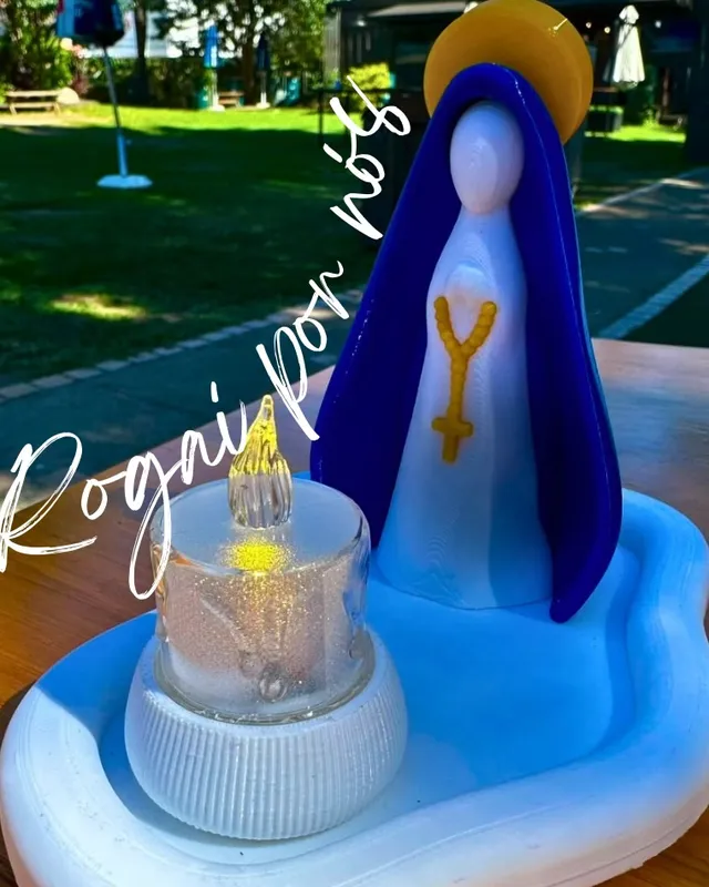 Imagem estilizada de Nossa Senhora em azul com vela, ao ar livre